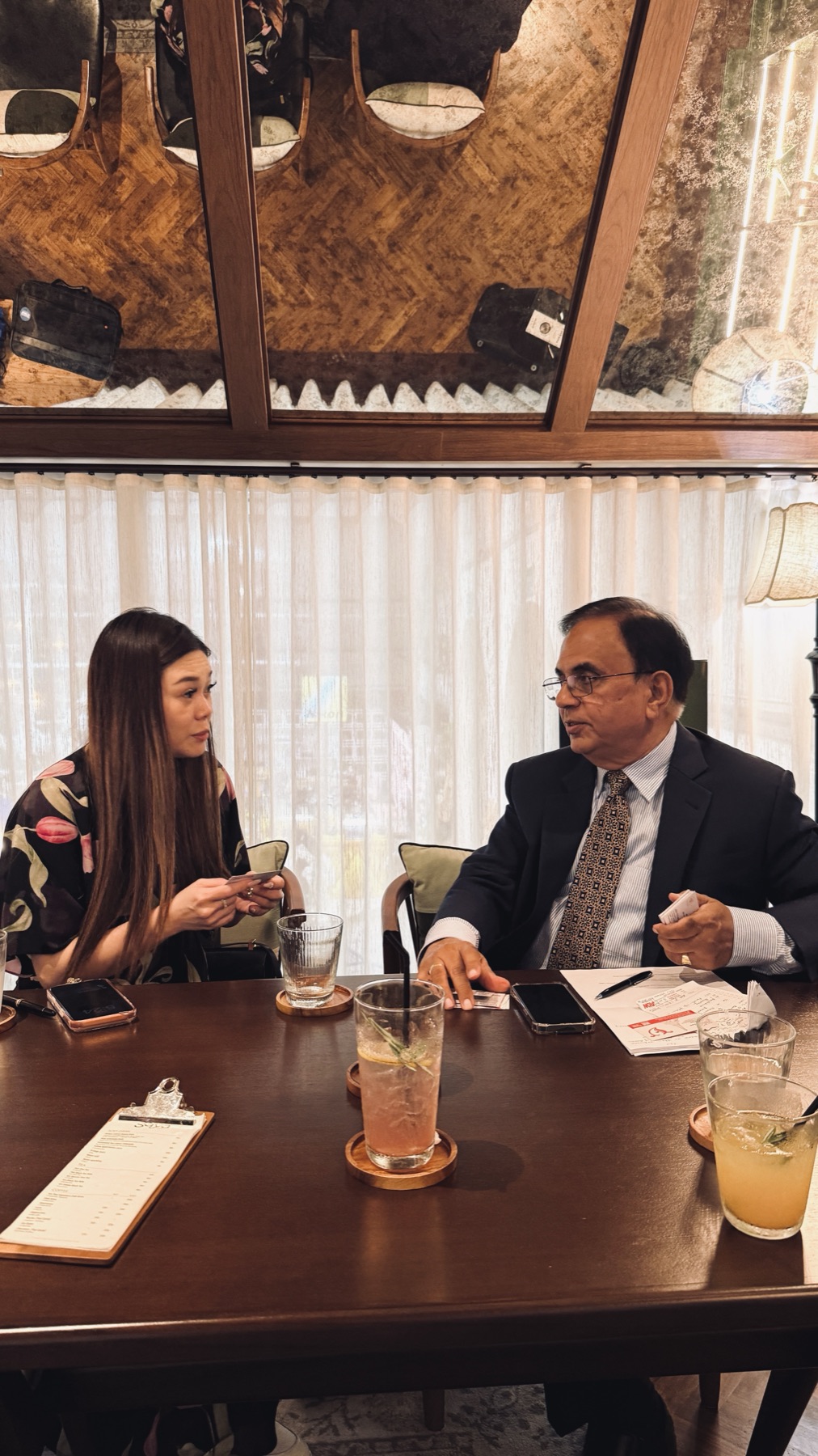 Two people in conversation over business cards and drinks at a restaurant lounge table