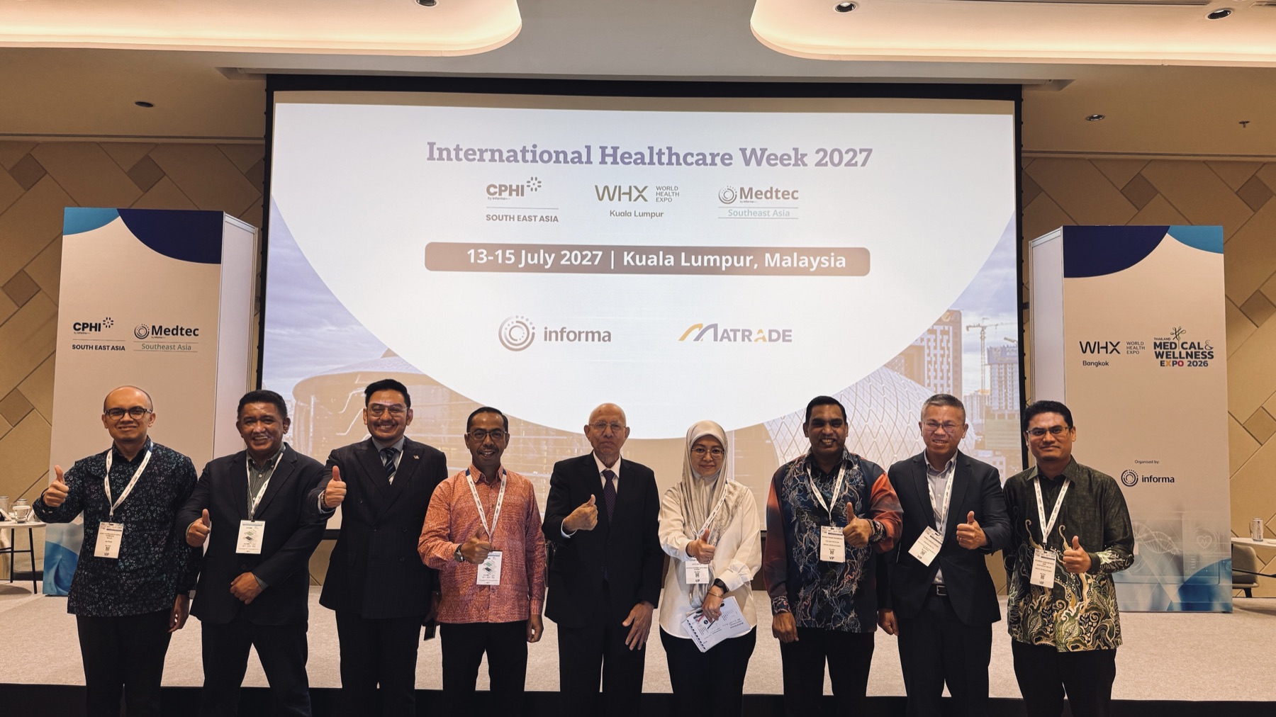 A delegation posing in front of a screen announcing International Healthcare Week 2027 in Kuala Lumpur, Malaysia