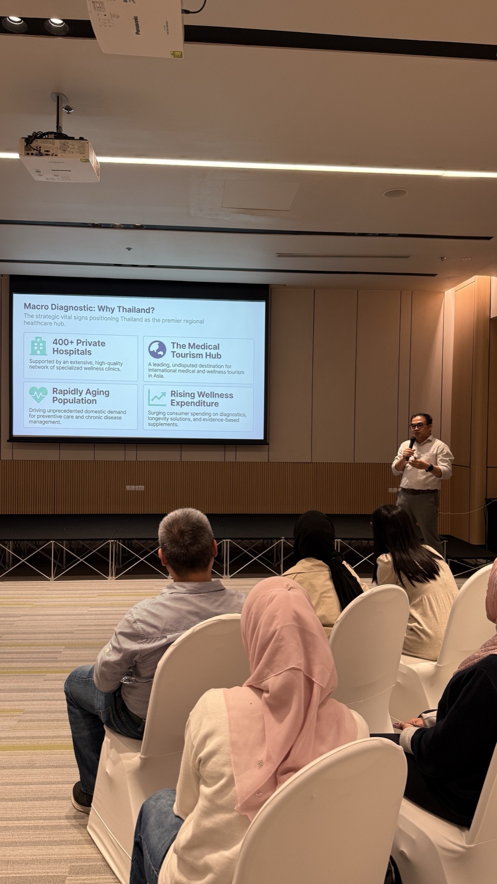 A presenter on stage in front of a slide titled 'Macro Diagnostic: Why Thailand?' with an audience seated in rows
