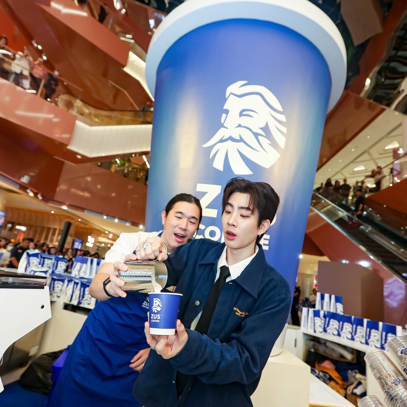 Two performers pouring milk into a branded coffee cup in front of a giant cup backdrop at a mall activation