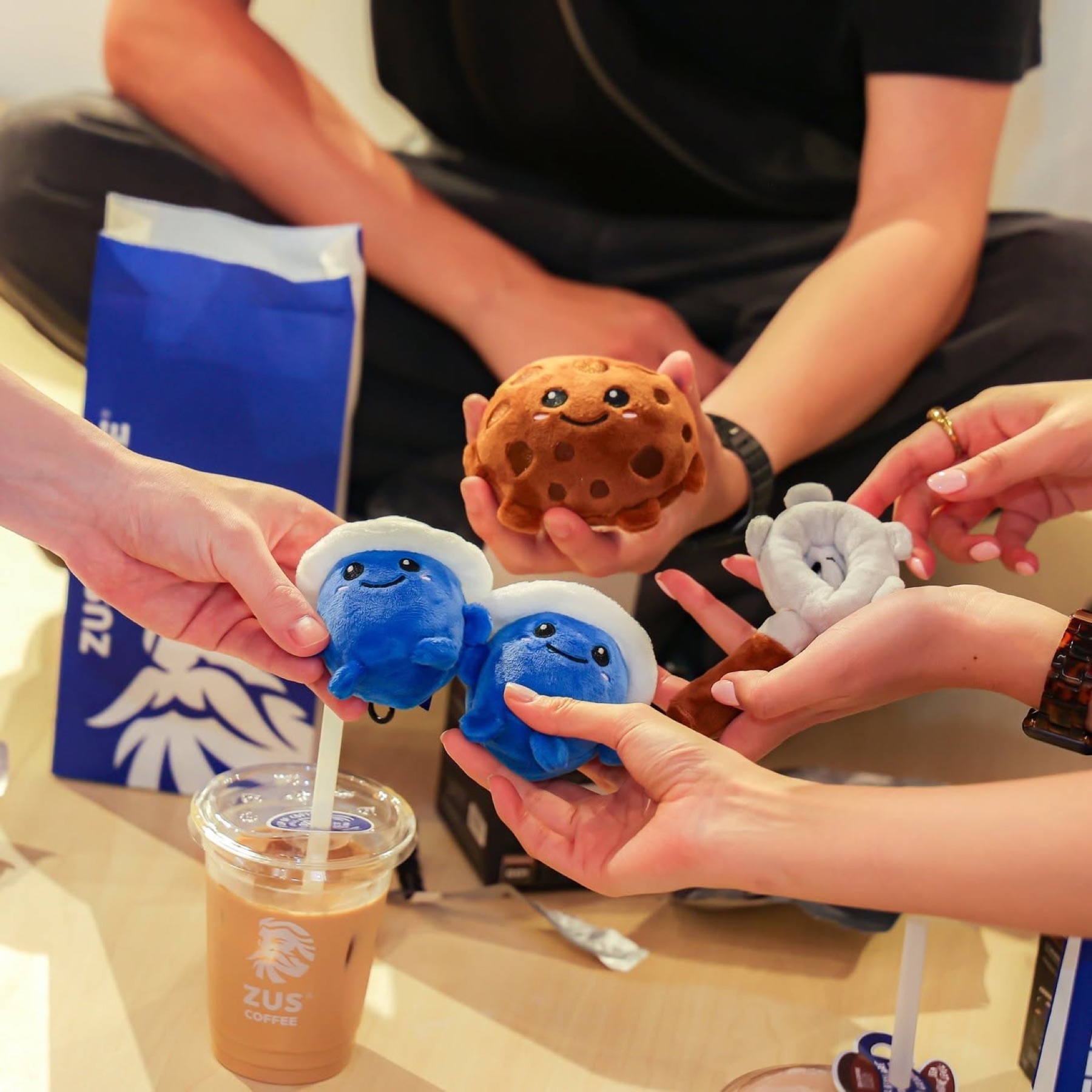 Hands holding plush toy mascots and an iced coffee cup, a close-up lifestyle content moment