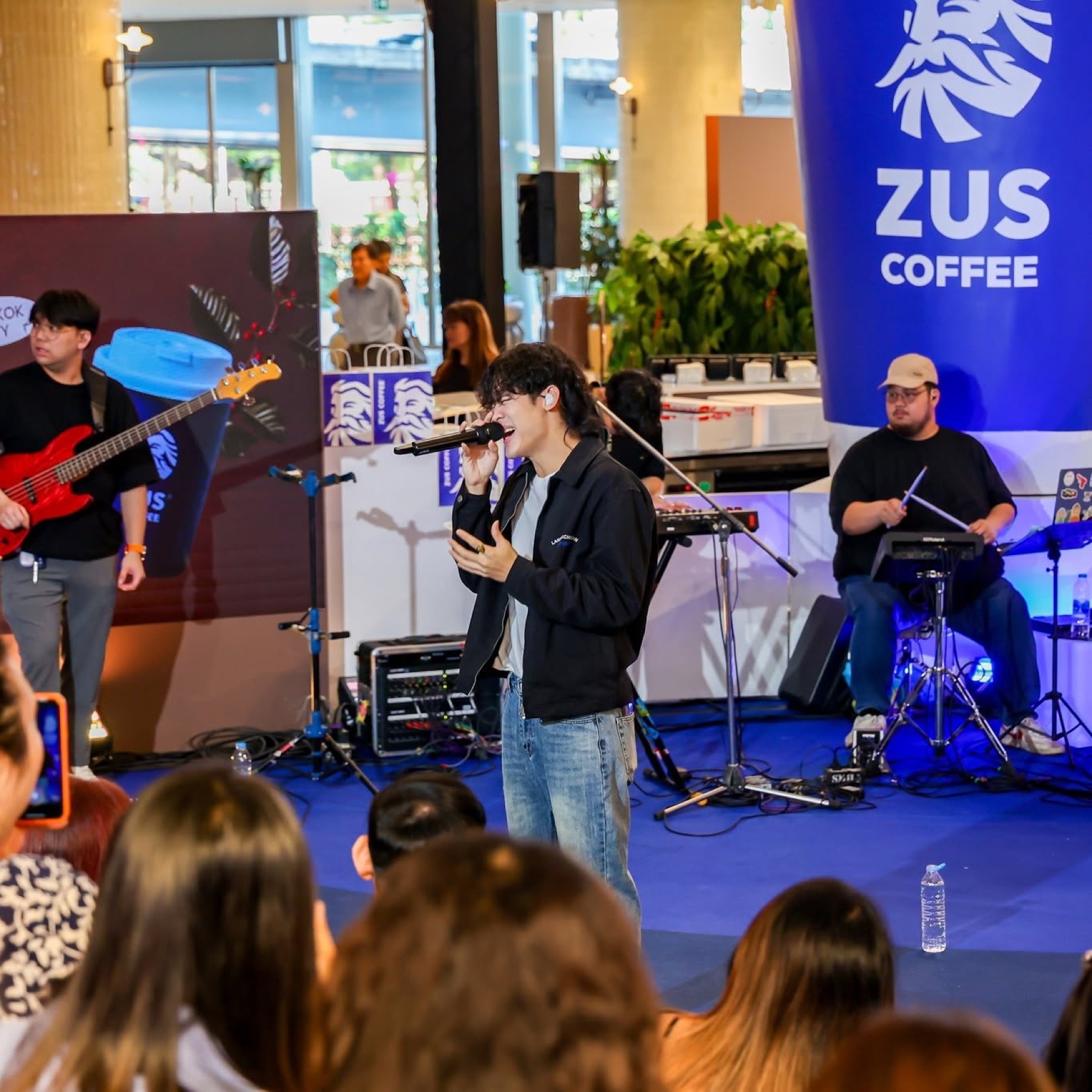 A singer performing on stage with a live band at a coffee brand launch event